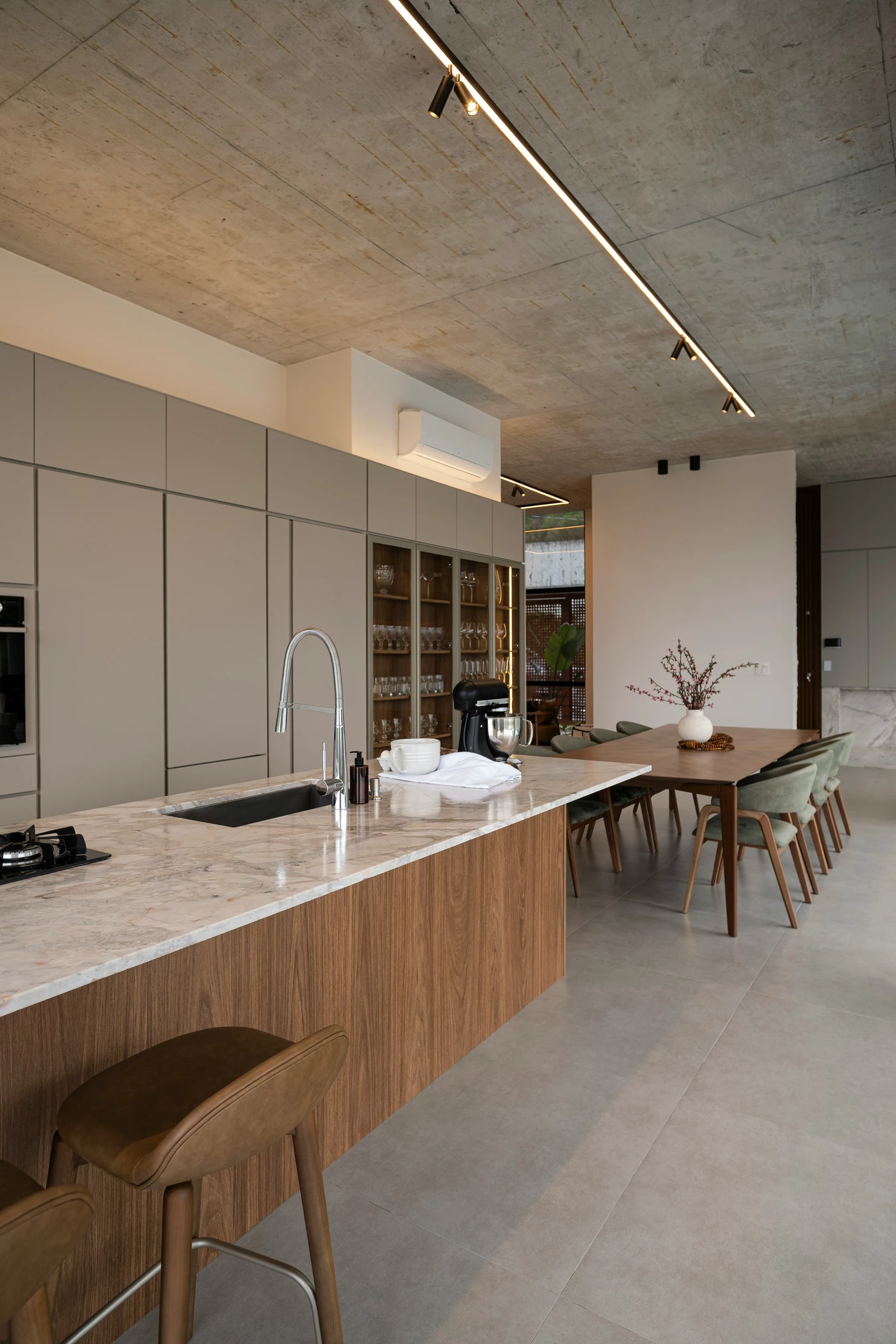 A kitchen with a marble island on a walnut base under a concrete ceiling